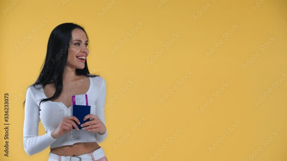 Smiling girl pointing with finger at passport and air ticket isolated on yellow Smiling girl pointing with finger at passport and air ticket isolated on yellow