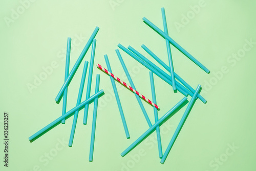 Paper straw among with pile plastic straws on green background photo