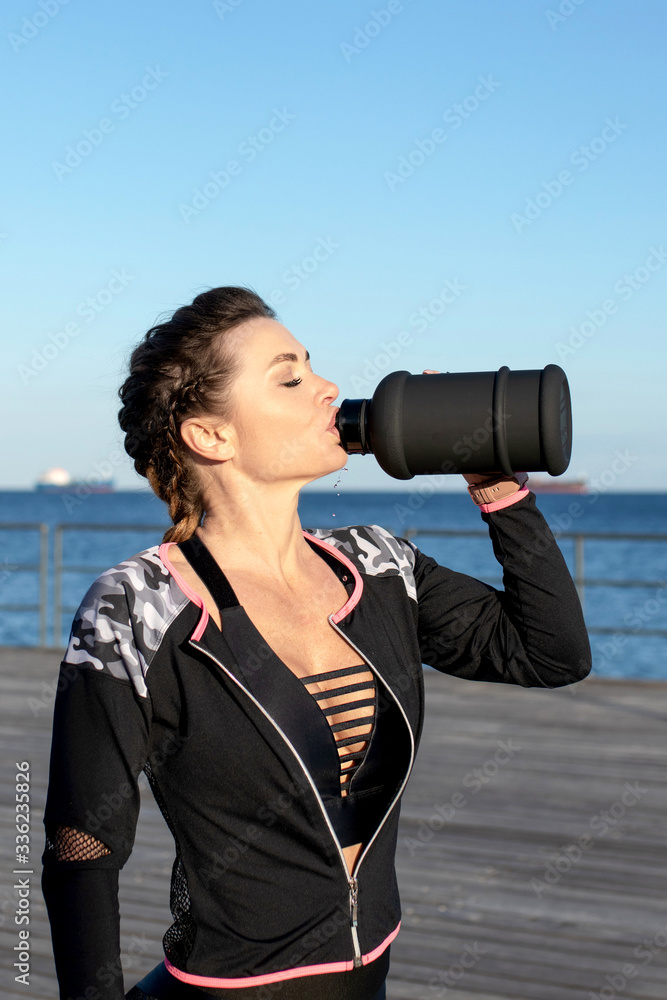 Caucasian female fitness model drinking from a bottle during exercise outdoor at a sea promenade