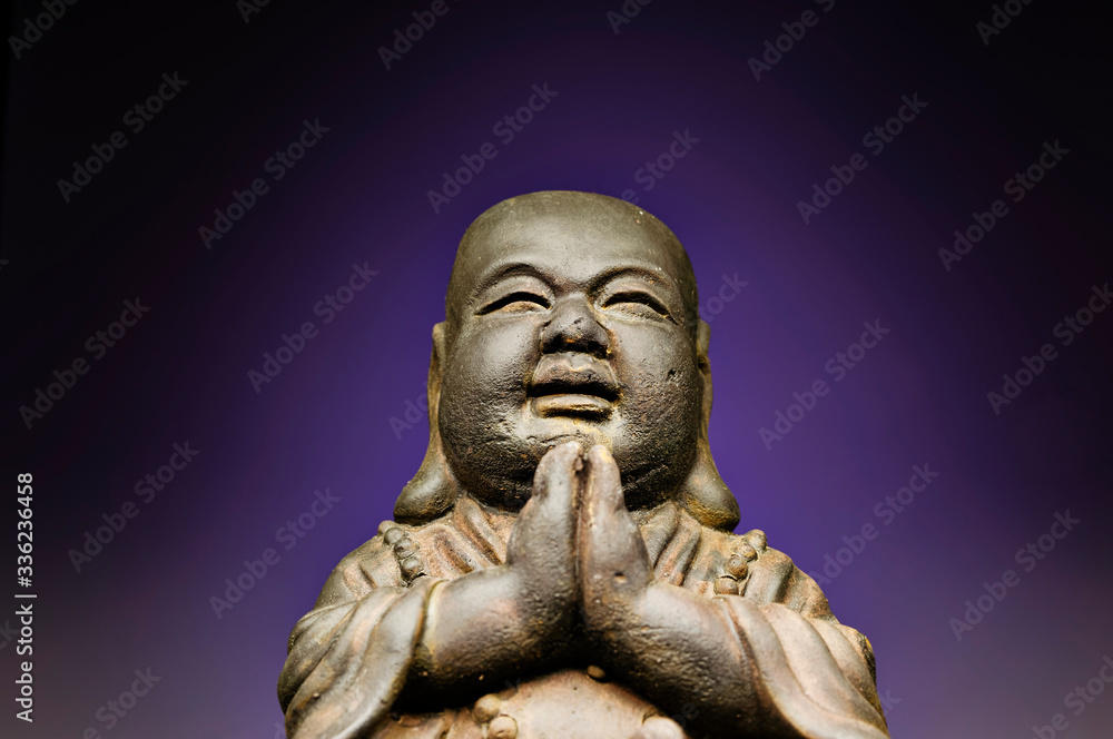 A small replica statue of The Buddha with a green background.  Purple representing divinity and immortality