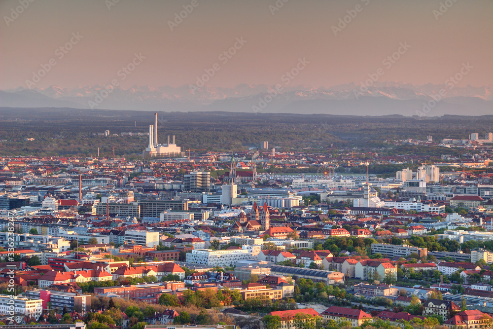 Aerial view of modern European city outskirts in evening light with industrial, commercial and residential buildings, power plant with chimneys and Bavarian Alps in background, Munchen Bayern Germany