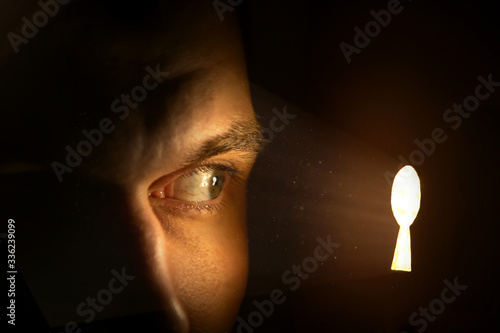 A curious man looks with one eye into a luminous keyhole. Side view. Background for text or design. Banner design.	