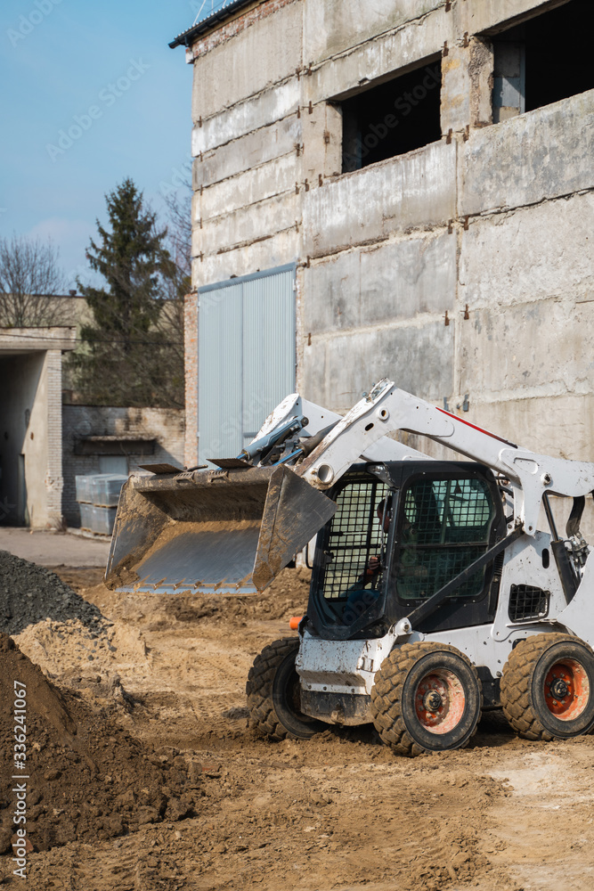 White skid steer loader at a construction site working with a soil. Industrial machinery. Industry.
