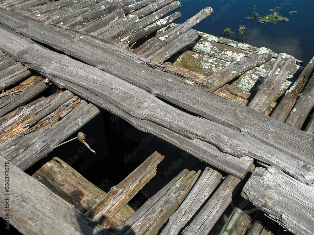 Close-up of old wooden bridge over a small river in summer sunny day time. Blue sky and white clouds reflection on water