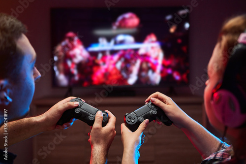 Portrait of crazy playful couple, Gamers enjoying Playing Video Games on Playstation indoors sitting on the sofa, holding Console Gamepad in hands, Xbox fans. Resting At Home, have a great Weekend