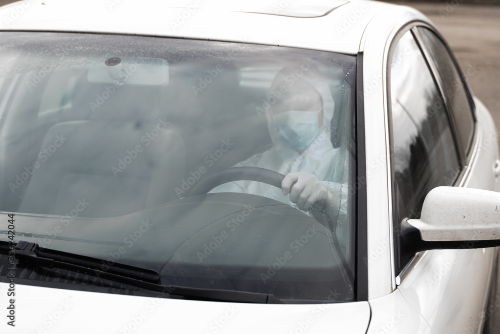 Man in protective suit, medical mask and rubber gloves for protect himself from bacteria and virus is driving car. Protective mask while quarantine, world pandemic, covid 19, coronavirus, infection. Man in protective suit, medical mask and rubber gloves for protect himself from bacteria and virus is driving car. Protective mask while quarantine, world pandemic, covid 19, coronavirus, infection.