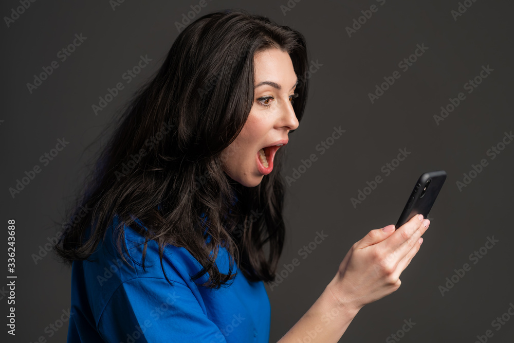 Angry woman screaming down, swears with somebody. Using mobile phone. Stressed and depressed mature lady on grey background Angry woman screaming down, swears with somebody. Using mobile phone. Stressed and depressed mature lady on grey background
