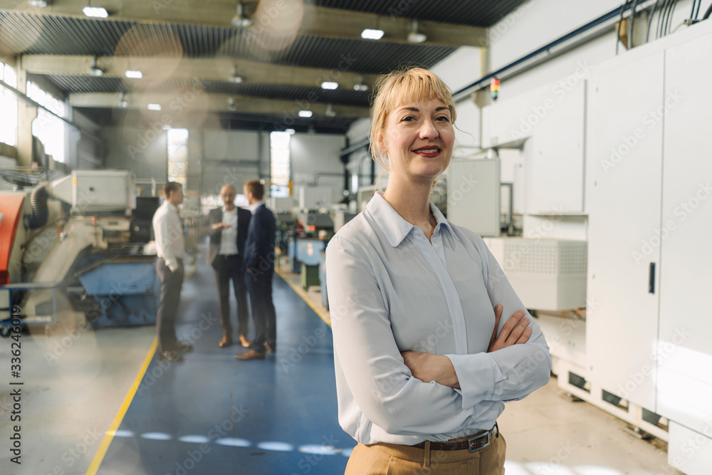 Portrait of a confident businesswoman in a factory with colleagues in backgound Portrait of a confident businesswoman in a factory with colleagues in backgound