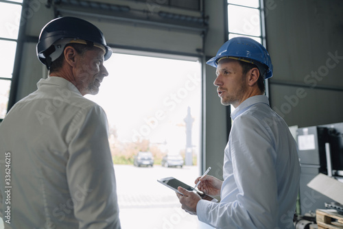 Two men wearing hard hats talking in a factory photo