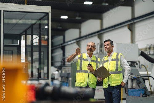 Two men in reflective vests talking in a factory