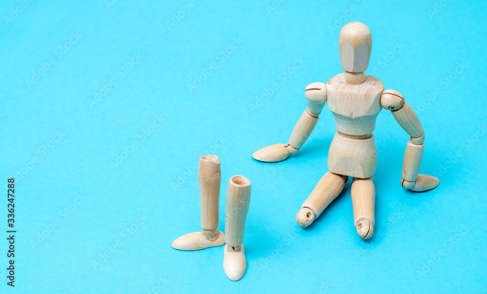 Wooden man mannequin sits without legs on a blue background. The concept of prostheses. Wooden man mannequin sits without legs on a blue background. The concept of prostheses.