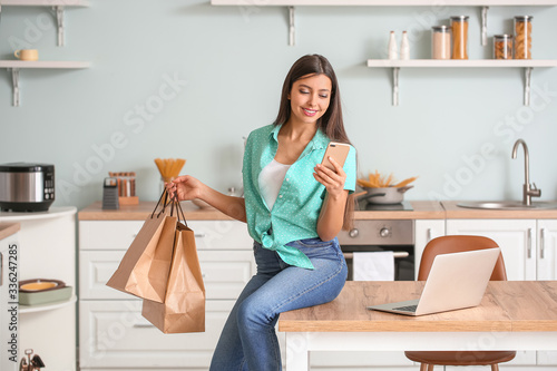 Young woman with mobile phone and shopping bags at home