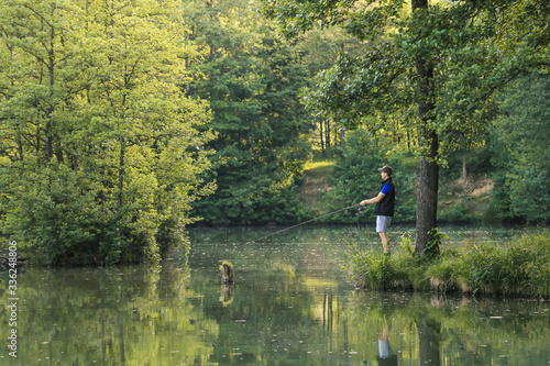 Man fishing in the green wilderness with lush forest on a sunny summer day at sunset. © 24K-Production