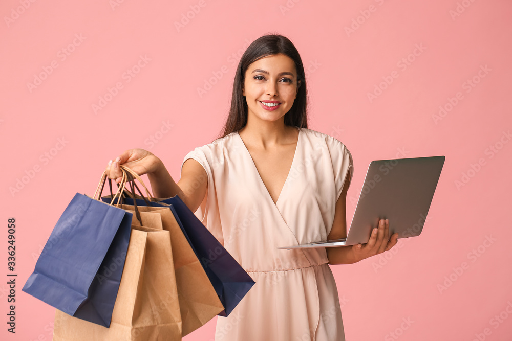 Young woman with laptop and shopping bags on color background