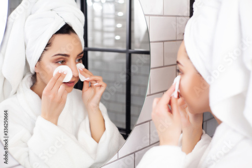 Cute woman in white coat and towel on her head makes herself a makeup