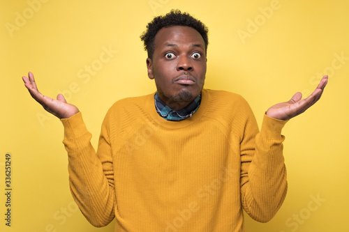 Young african man in yellow clothes shrugging shoulders