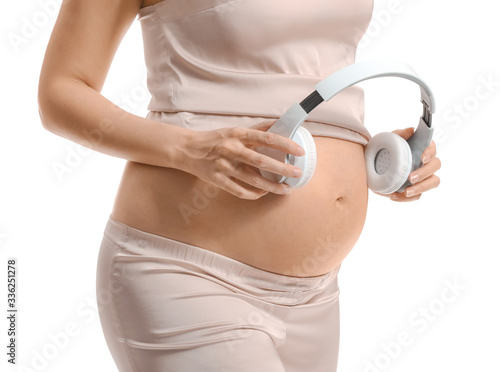 Beautiful pregnant woman with headphones on white background