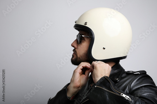 Close-up side portrait of young bearded biker man with white cafe-racer helmet. White background.