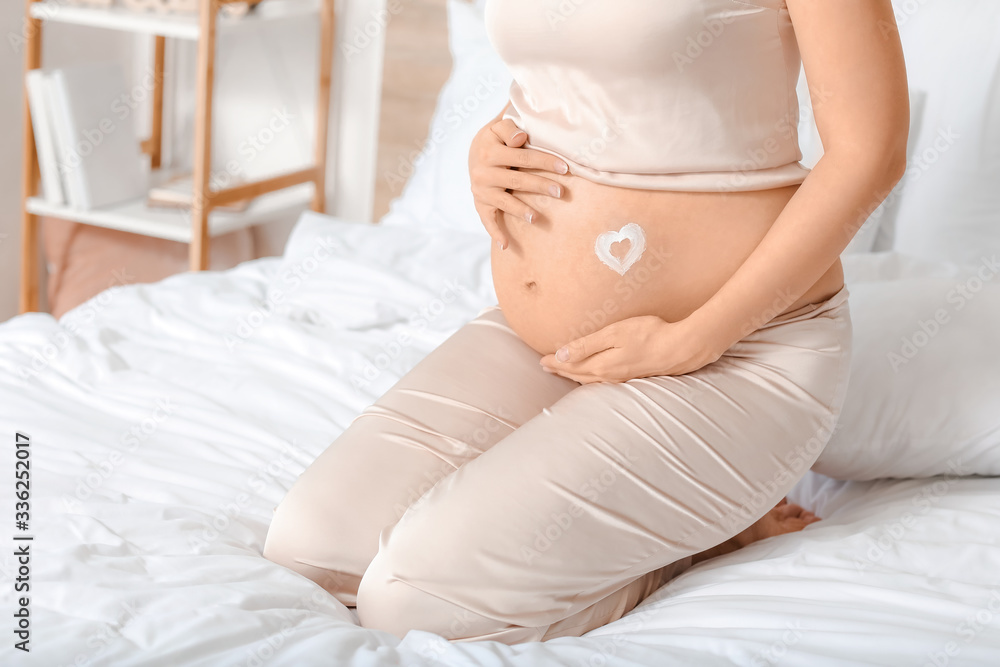 Beautiful pregnant woman applying body cream in bedroom Beautiful pregnant woman applying body cream in bedroom