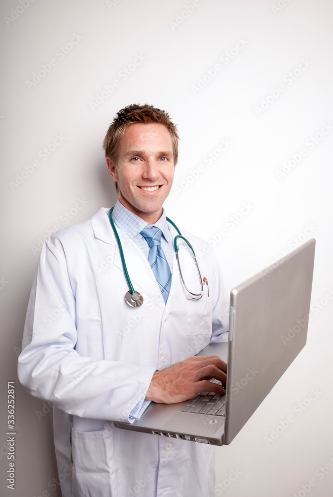 Friendly doctor in white lab coat and stethoscope smiling holding his laptop computer Friendly doctor in white lab coat and stethoscope smiling holding his laptop computer