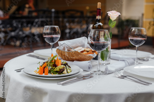 served table for four with a bottle of wine  glasses  bread  salad with carrots  outdoors