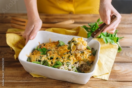 Baked chicken thigh fillet with rice, with cheese crust and soy sauce. Long-grain rice and green bean. White baking dish casserole on a wooden table, yellow fabric napkin, parsley leaves. Hold a dish