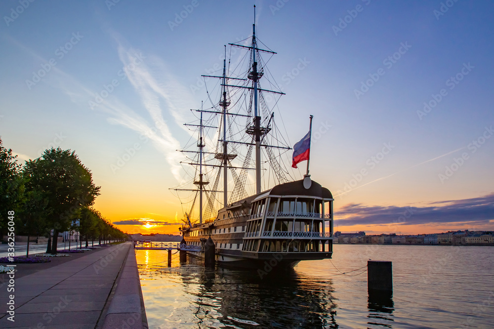 Saint Petersburg. Russia. Vintage frigate on the banks of the Neva. Ship off the coast of St. Petersburg. Flag of Russia is fixed on a vintage frigate. Bridge to go to the ship. Sunset in Petersburg