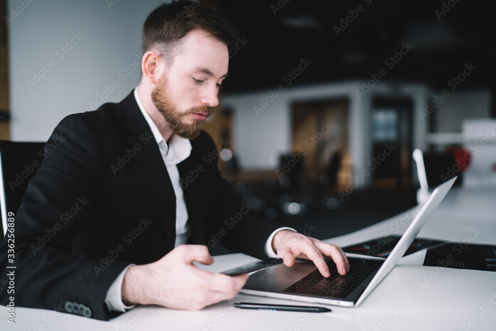 Focused businessman in office typing on laptop and browsing mobile Focused businessman in office typing on laptop and browsing mobile