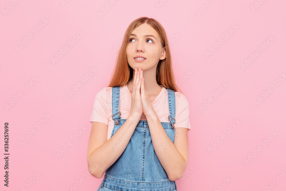A young cheerful girl with hope prays on an isolated pink background A young cheerful girl with hope prays on an isolated pink background
