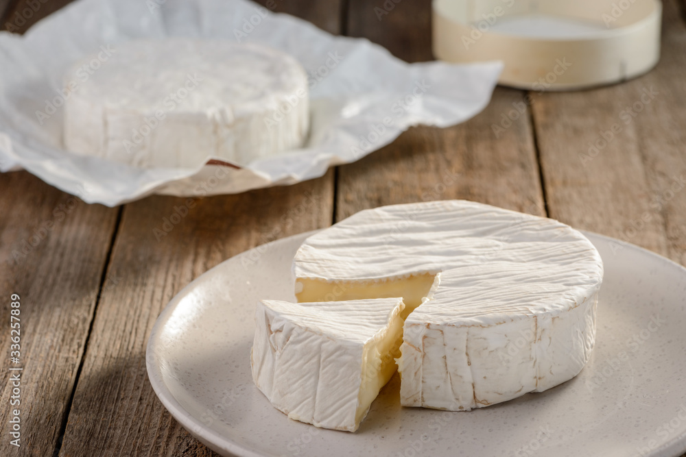 Fresh Camembert cheese on a white plate on wooden background