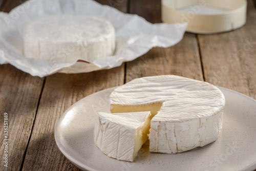 Fresh Camembert cheese on a white plate on wooden background