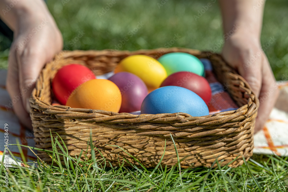 Female hands hold multi-colored Easter eggs in a basket on the grass, the background is blurred, shallow depth of field, selective focus. Easter holiday concept Female hands hold multi-colored Easter eggs in a basket on the grass, the background is blurred, shallow depth of field, selective focus. Easter holiday concept