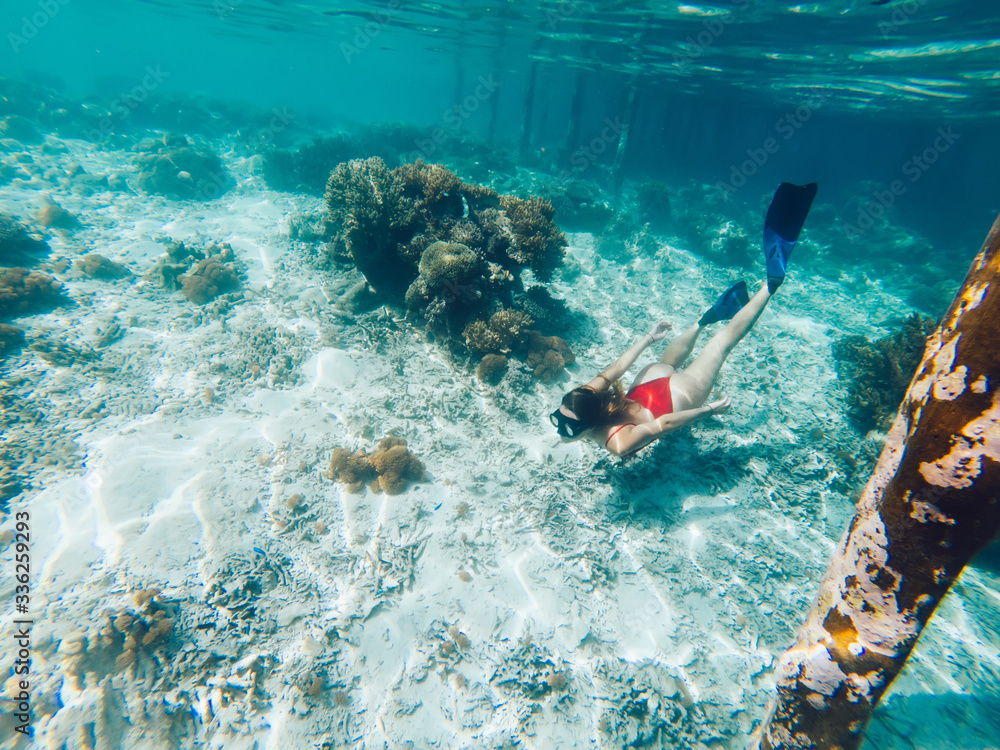 Young girl with diving mask and snorkel flippers in clear blue sea water, woman in red bikini swims in turquoise crystal transparent ocean water, tropical coral reef snorkeling on summer holidays