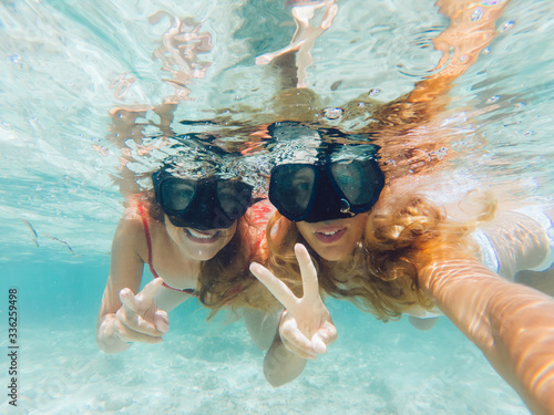 Young smiling female couple taking selfie and showing victory gesture underwater