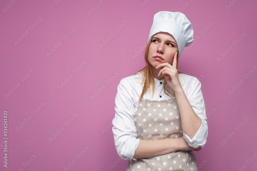 beautiful thoughtful girl cook in uniform and apron on a colored pink background, woman housewife in kitchen clothes thinks and dreams beautiful thoughtful girl cook in uniform and apron on a colored pink background, woman housewife in kitchen clothes thinks and dreams