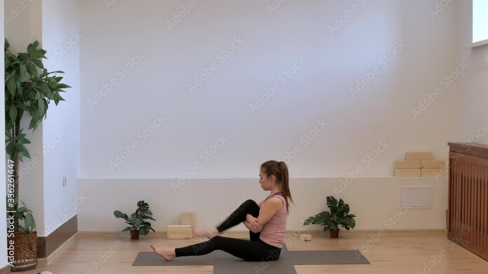 The girl in the yoga room does a knee warm-up sitting on a yoga mat. The girl in the yoga room does a knee warm-up sitting on a yoga mat.