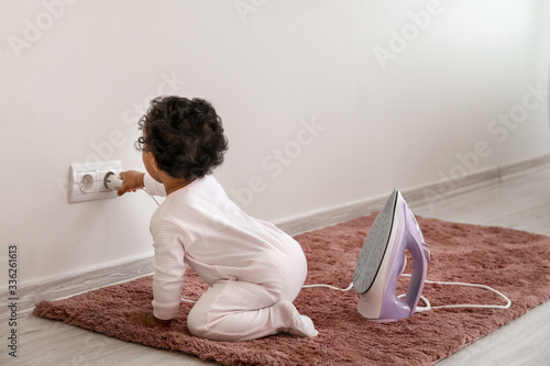 Tableau sur toile Little African-American baby playing with socket and iron at home