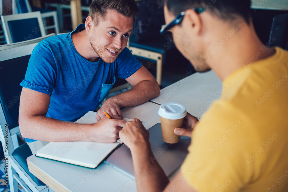 Fototapeta premium Cheerful male writing note doing project with partner in cafe