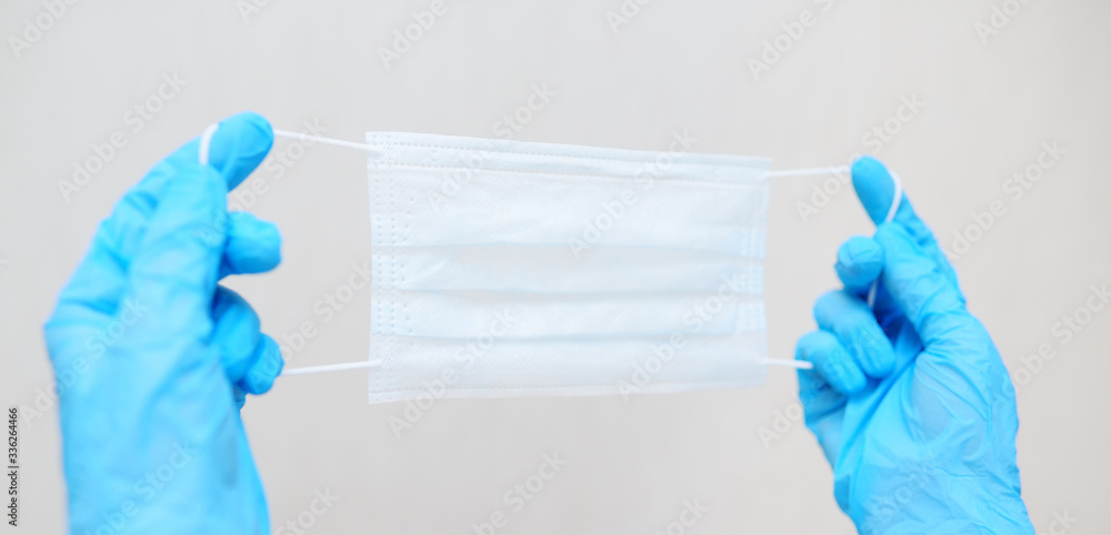 Fototapeta premium medical mask in the hands of a doctor in blue rubber gloves close-up on a light background. Hygiene, coronavirus, covid-19, airborne.