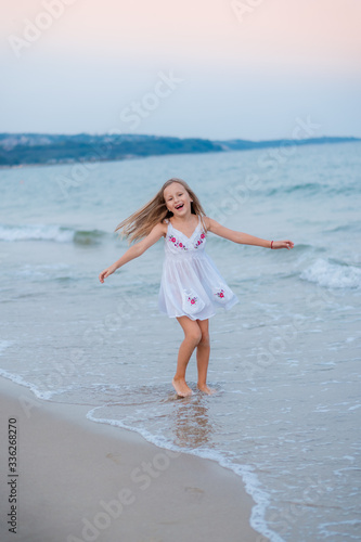 Girl blonde in a white dress runs on the waves of the sea and laughs at sunset