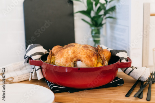 Hot and fresh oven-roasted whole chicken with lemon and garlic in a red dutch oven