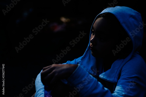 Sad girl in hoodie sitting in the dark with face lit by moonlight photo