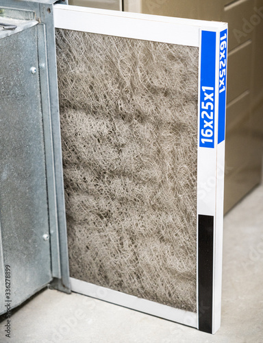 Old dirty furnace filter partially removed from holder