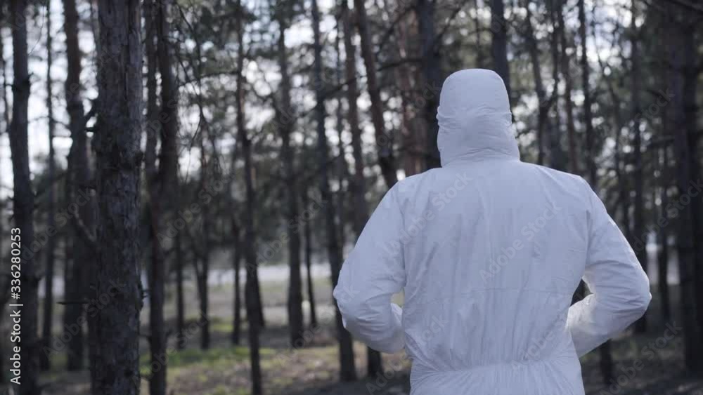 Back view of young Caucasian man in white safety suit, protective eyeglasses and face mask running in sunny spring park. Lifestyle of sportsman during coronavirus quarantine. Pandemic, Covid-19. Back view of young Caucasian man in white safety suit, protective eyeglasses and face mask running in sunny spring park. Lifestyle of sportsman during coronavirus quarantine. Pandemic, Covid-19.