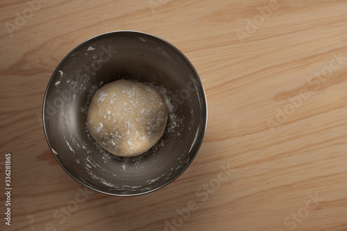 Overhead view of a ball of pizza dough with flour in an iron bowl on a wooden table