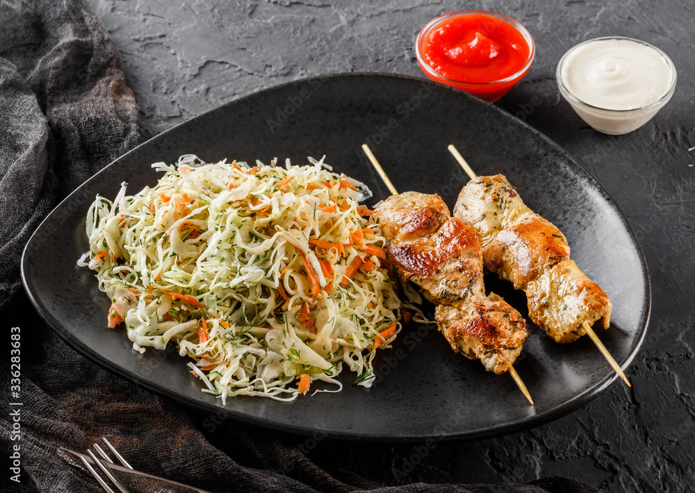 Grilled meat skewers with salad of cabbage and ketchup sauce on black stone background. Hot fast food dish, close up