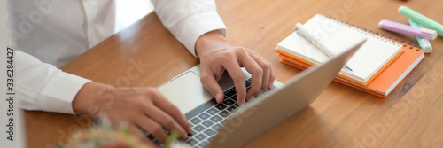 Cropped shot of young male university student typing on laptop on wooden table