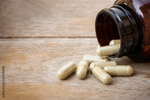 Green herbal capsules pill in brown glass bottle isolated on old wood table background.