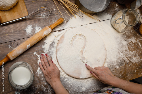 A Woman's hand draws symbols on the scattered flour. Baking cooking Ingredients flour eggs rolling pin milk. Top view. Delicious food, recipes, cooking, gastronomy, on a wooden table.
