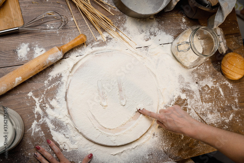 A Woman's hand draws symbols on the scattered flour. Baking cooking Ingredients flour eggs rolling pin milk. Top view. Delicious food, recipes, cooking, gastronomy, on a wooden table.